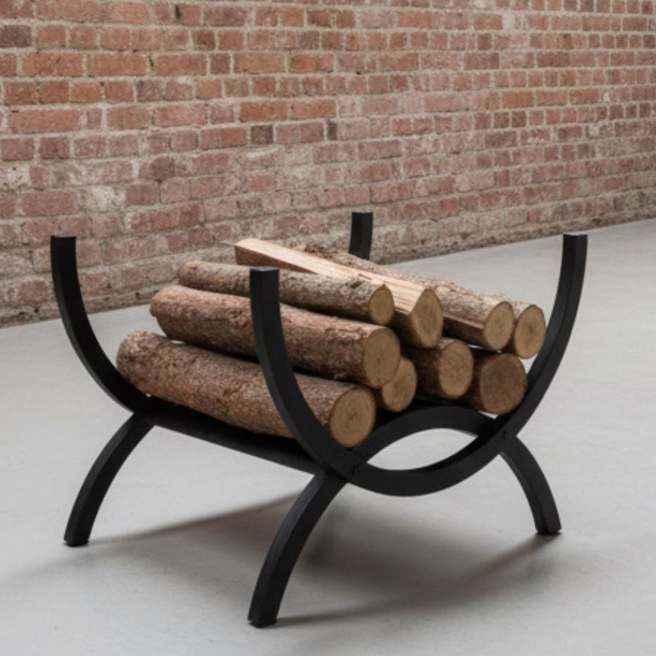 Fireplace firewood rack in black curved metal holding stacked logs in warm setting