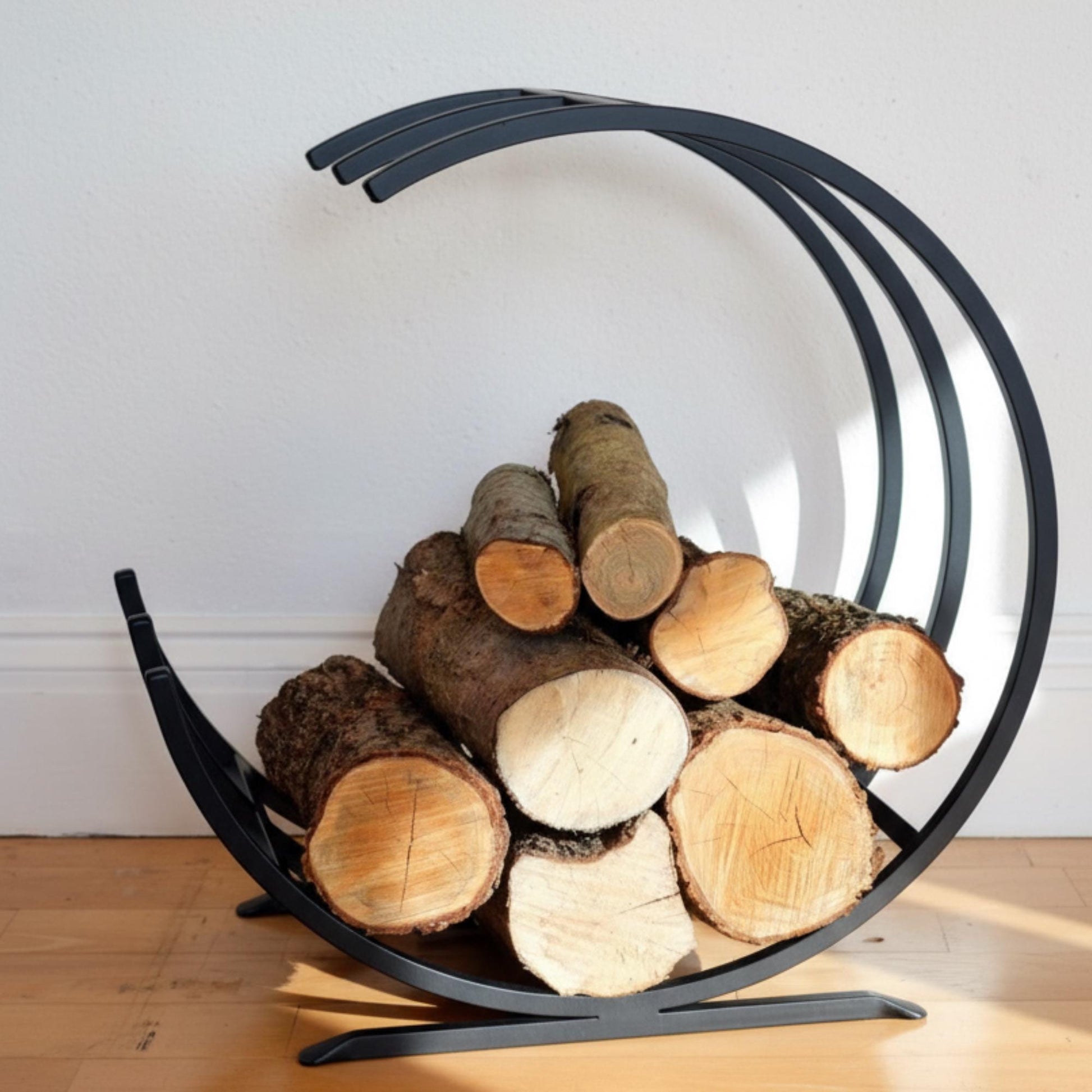 Black metal firewood holder with logs on a wooden floor against a white wall