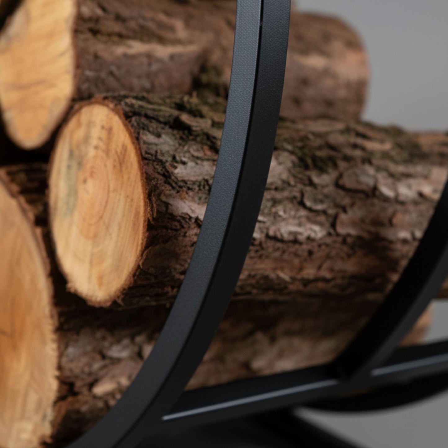 Round metal firewood rack with logs arranged for indoor use in living room or fireplace area